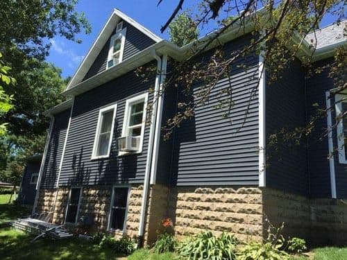 A house with new dark navy siding, white trim, and tan stone foundation.