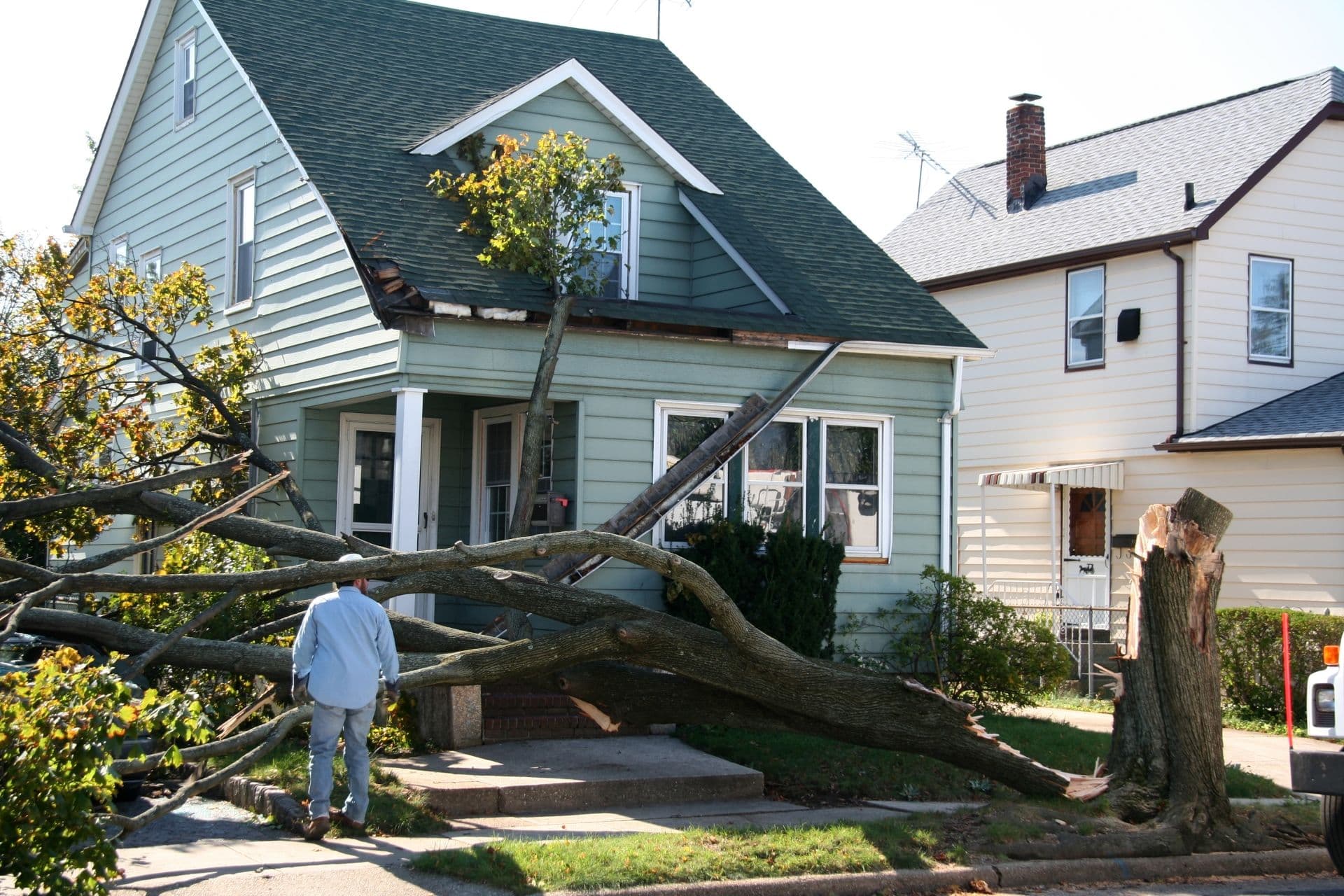A house with roof and gutter damage from a downed tree in a storm.