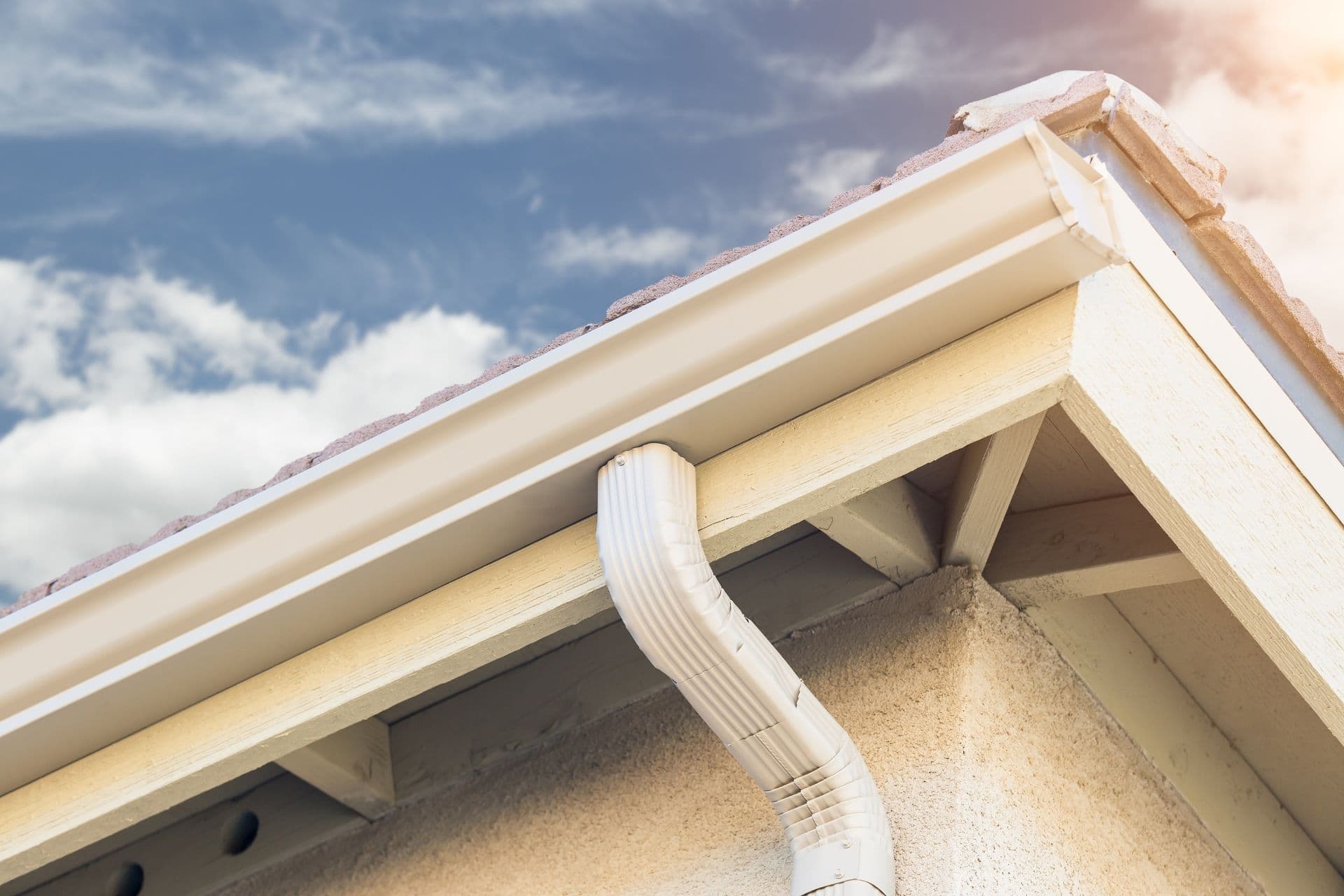 A close-up of new aluminum gutters on a house with blue sky visible in the background.