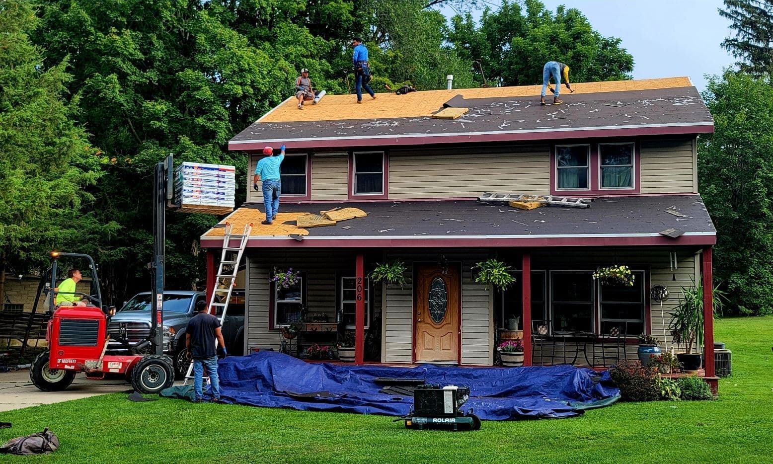 Workers install new roofing on a gray and red house.