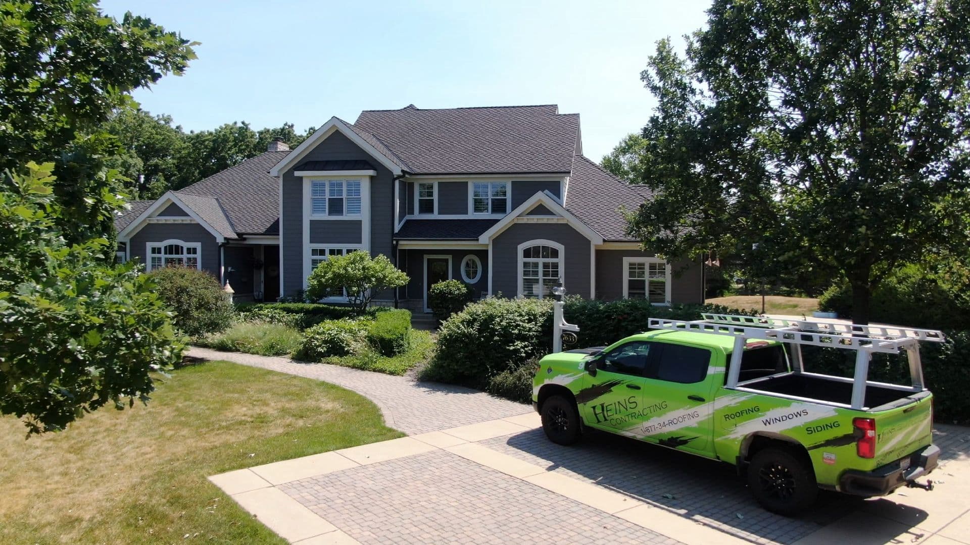 A Heins Contracting truck is parked in front of a gray house with white trim and an asphalt shingle roof.
