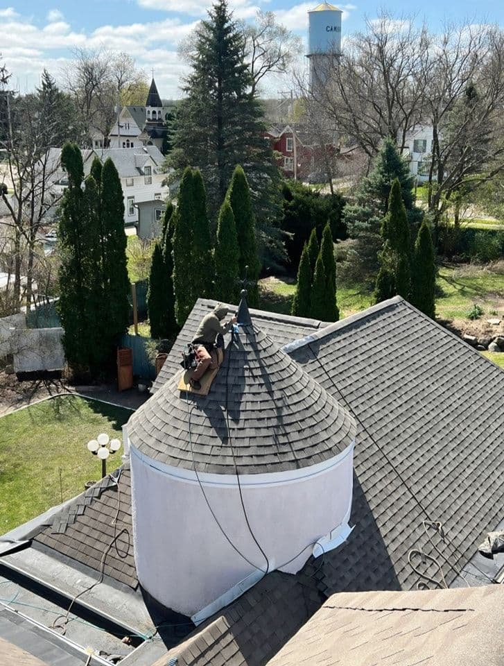 A worker installs roofing shingles on top of a cupola.