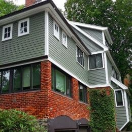 A house with red brick first floor and sage green vinyl siding on the second floor.
