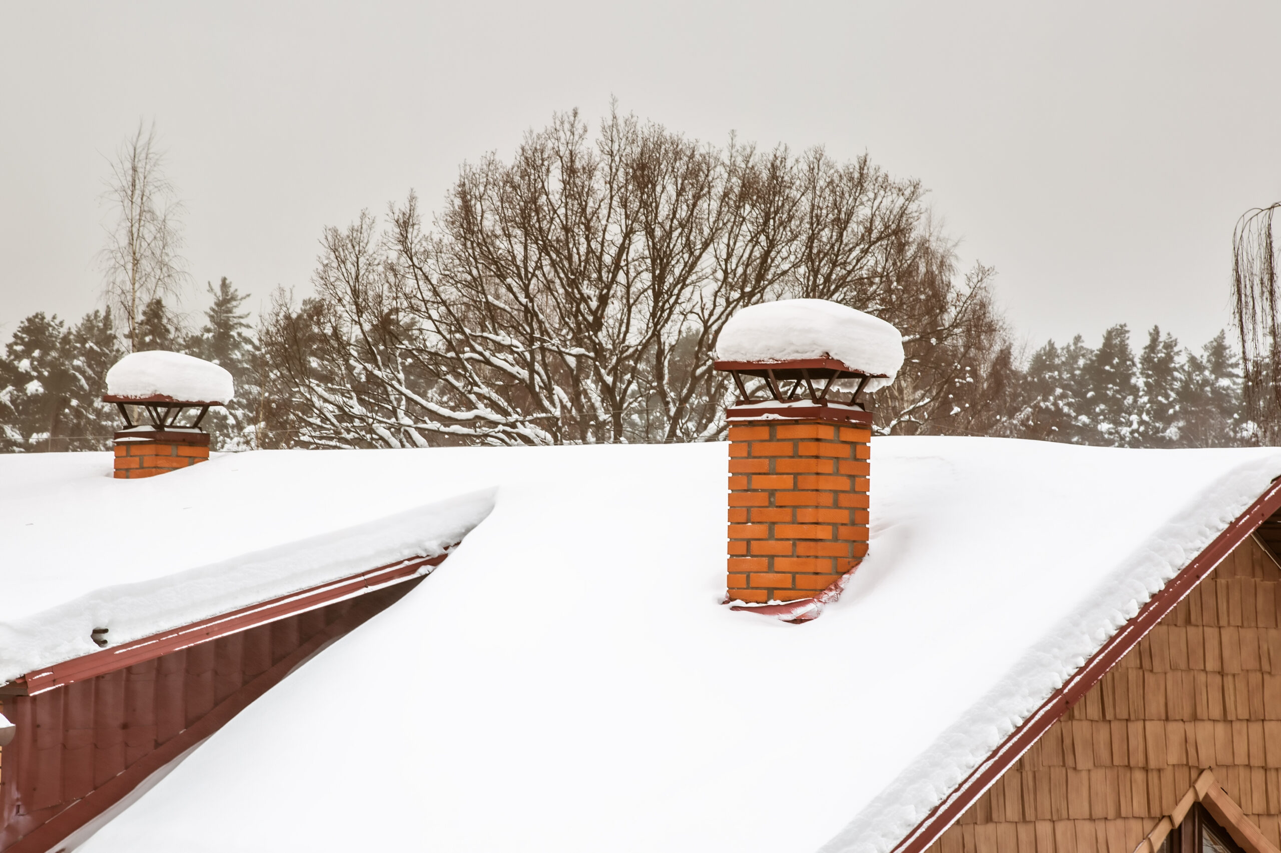 Two Red brick chimneys with iron chimney cap on the roof in snow